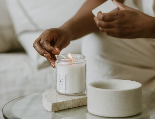 Woman lighting an Atmosphere Threesixty aromatherapy candle on her side table.